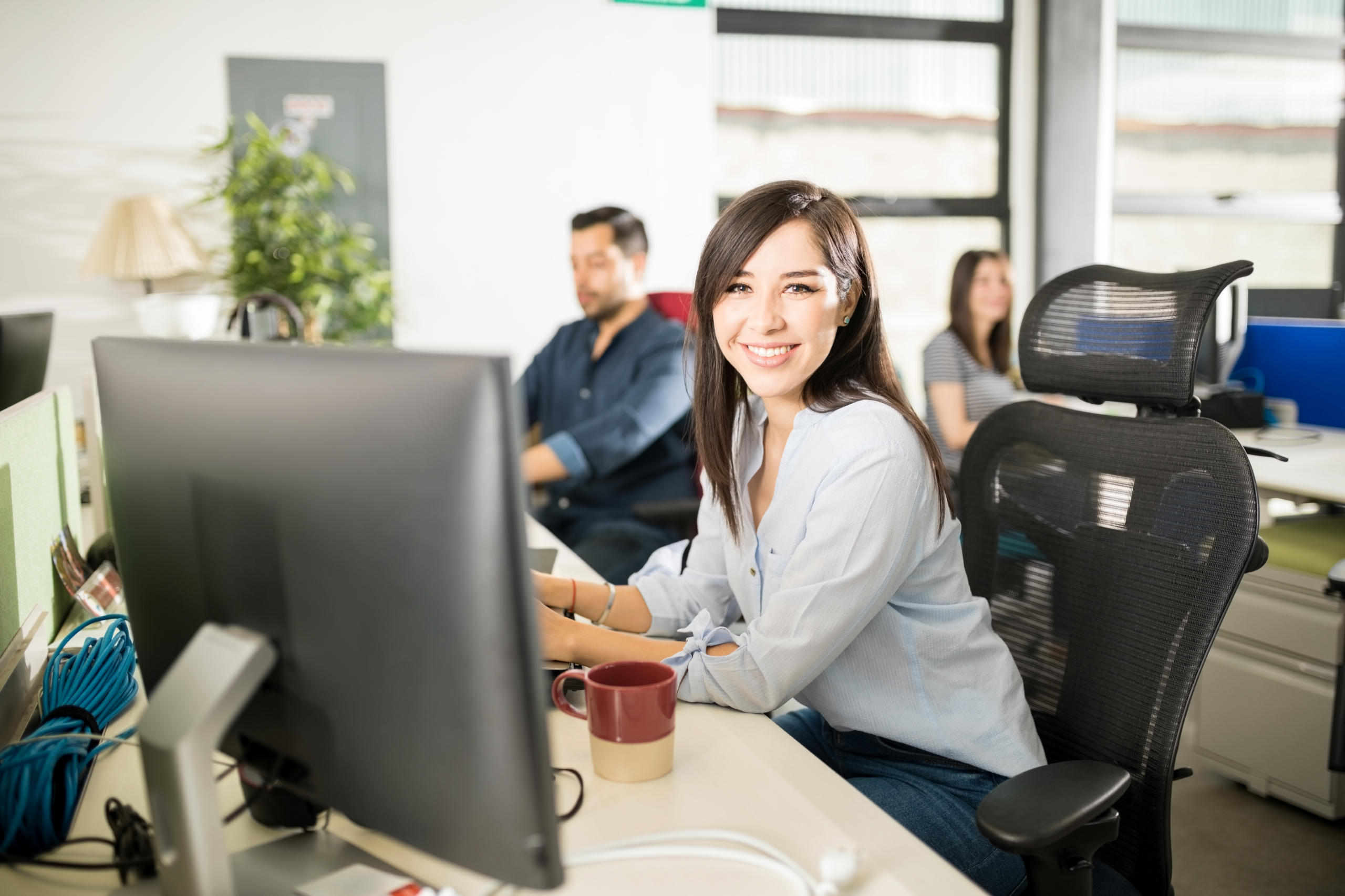 portrait smiling young latin woman sitting her desk with colleagues working back scaled